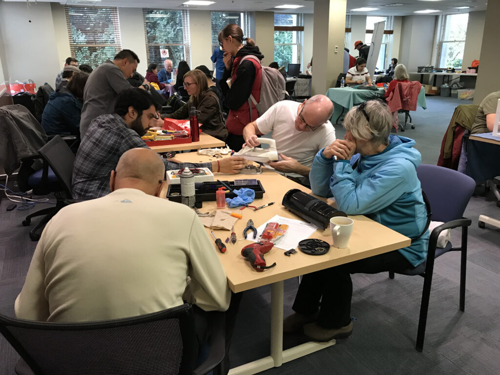 Fixers at work around a table. Repairing an iron and fan. Trout Lake Repair Cafe Oct 2019 attended by ElectroRecycle.