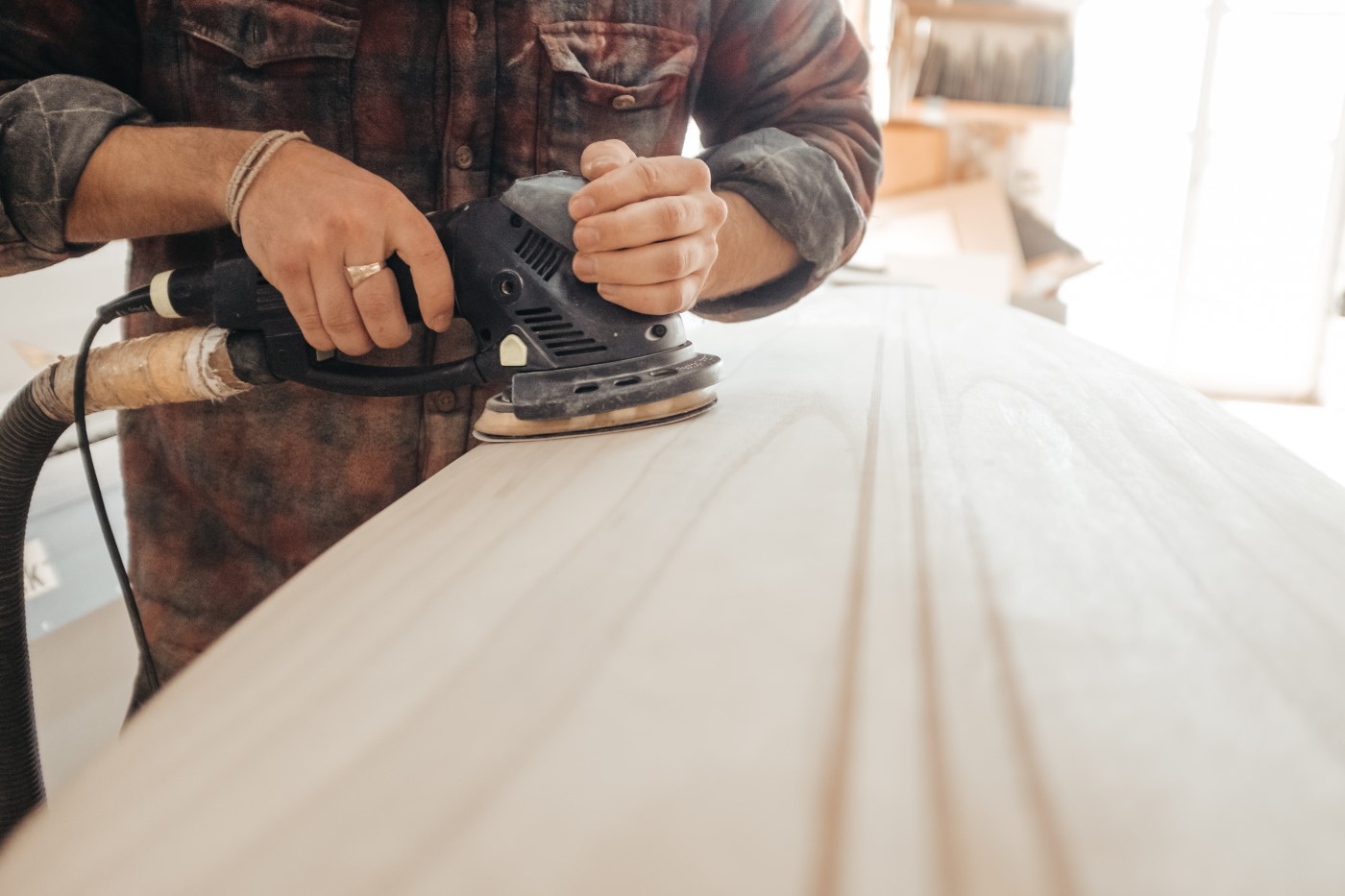 Man in plaid shirt using electric sander power tool on a board of wood.