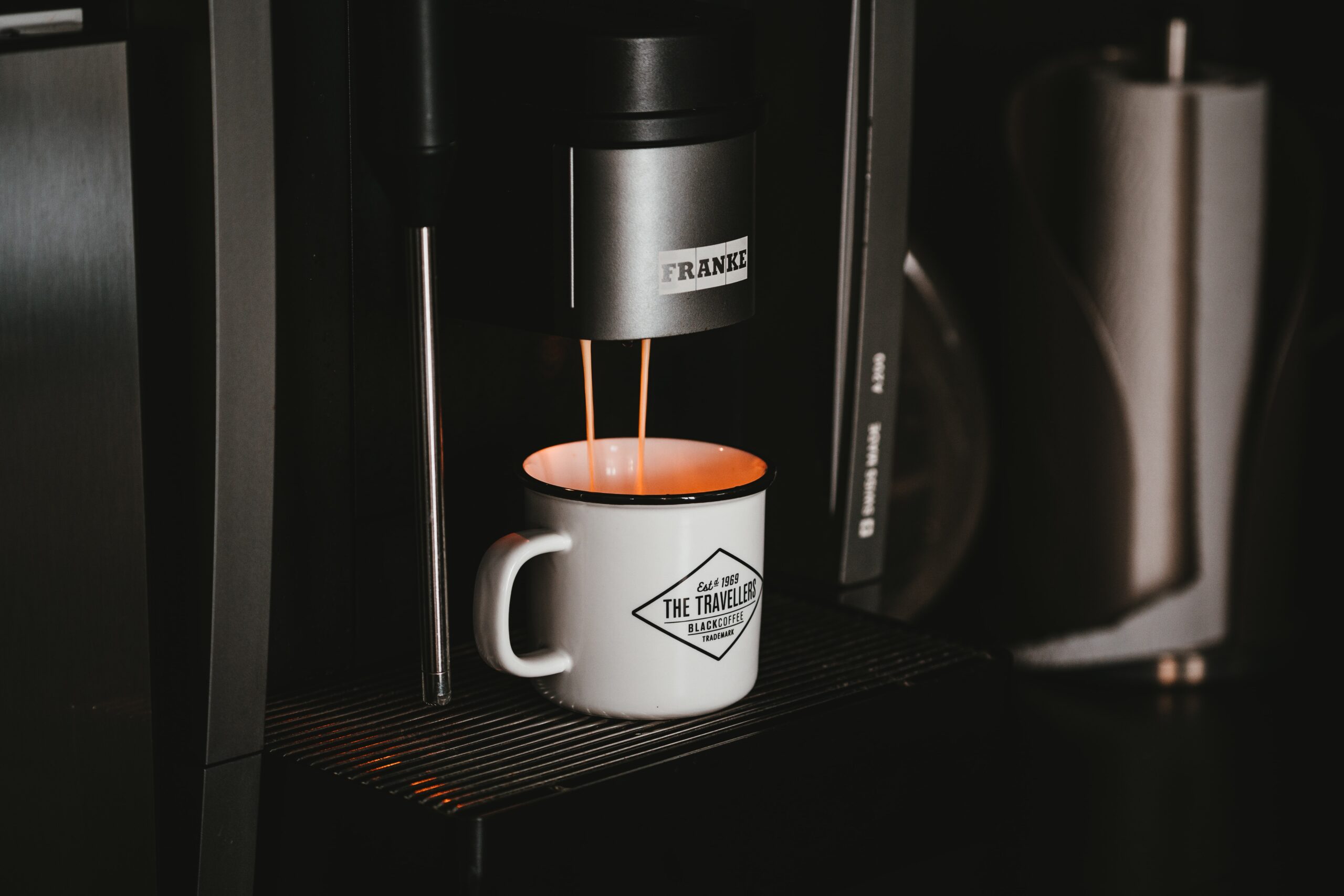White ceramic mug on black and silver coffee maker with espresso being brewed into the cup.