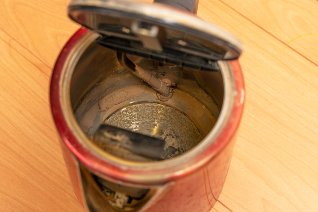 Top view of a broken old used electric kettle with scale and lime deposits on the bottom and heating element.